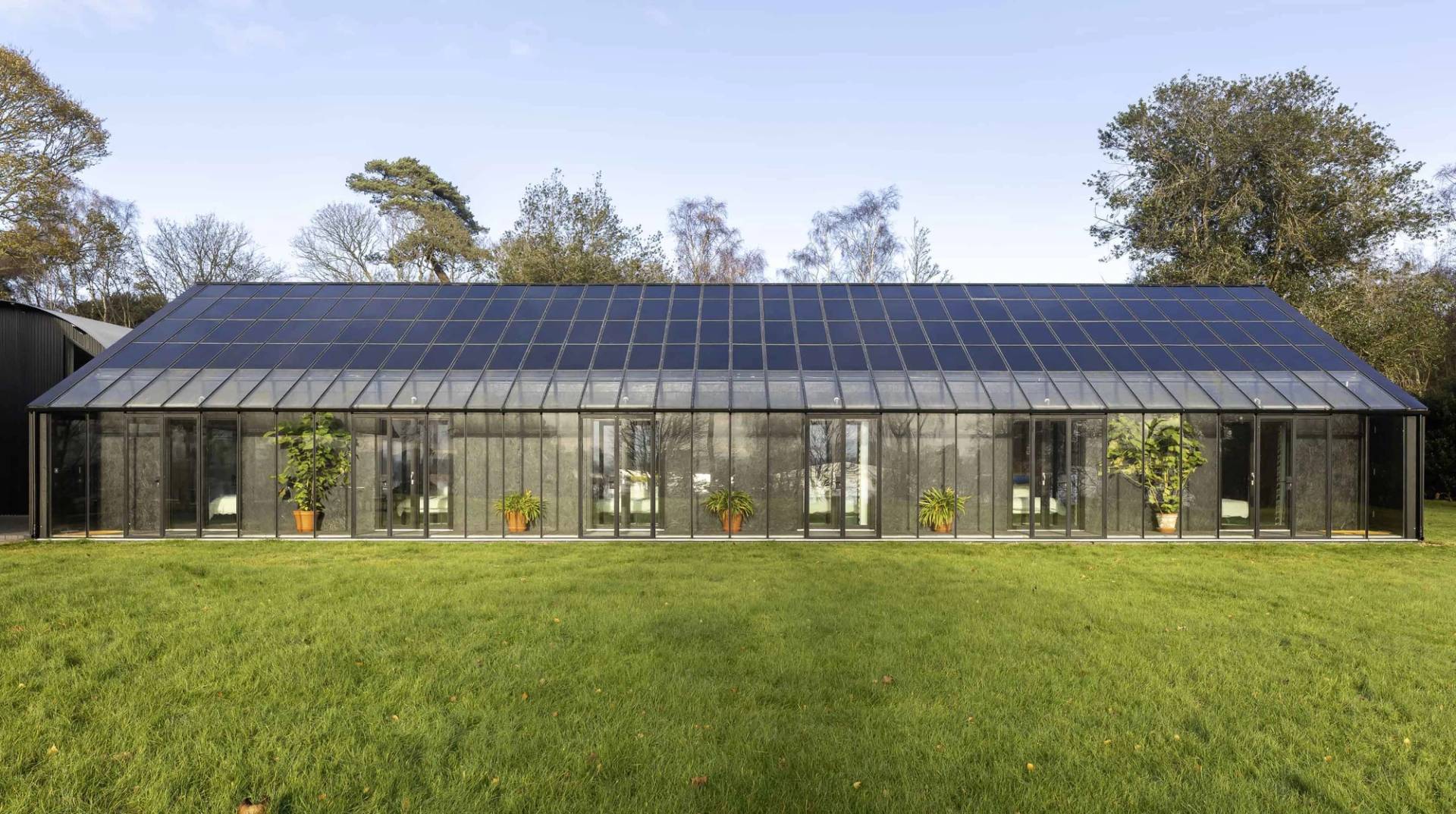 Long solar-panelled roof building with glass greenhouse facade set beside green lawns in Saxmundham, Love Locations IP17.