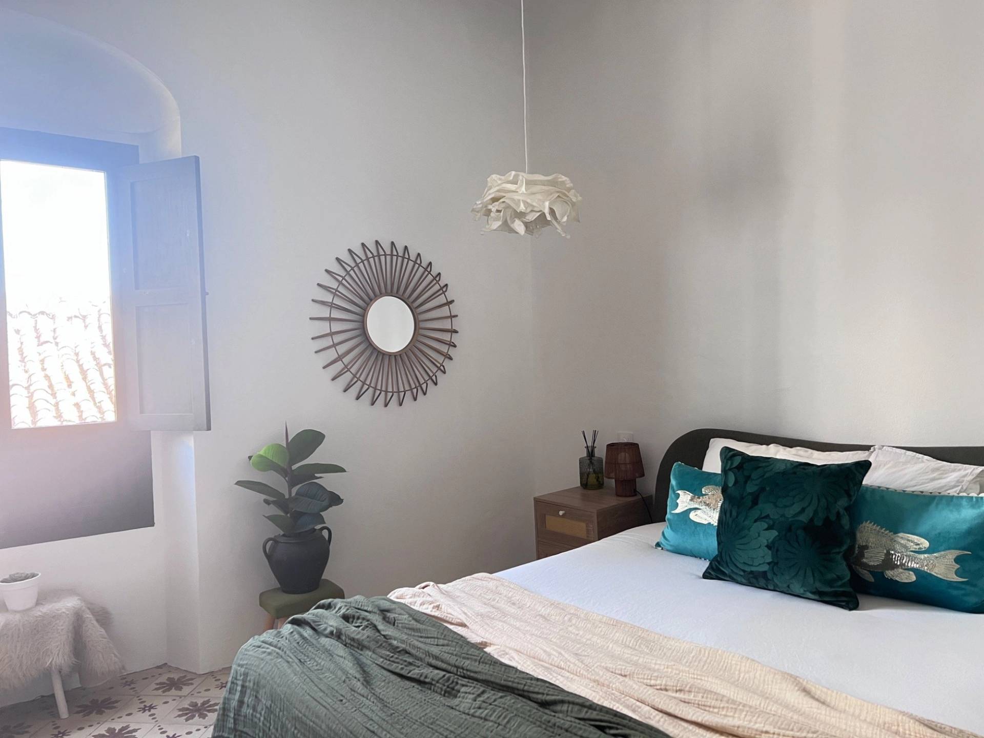 Minimalist bedroom location house in Jimena de la Frontera via Love Locations, showcasing a double bed with dark green bedding and a sunburst wall mirror.