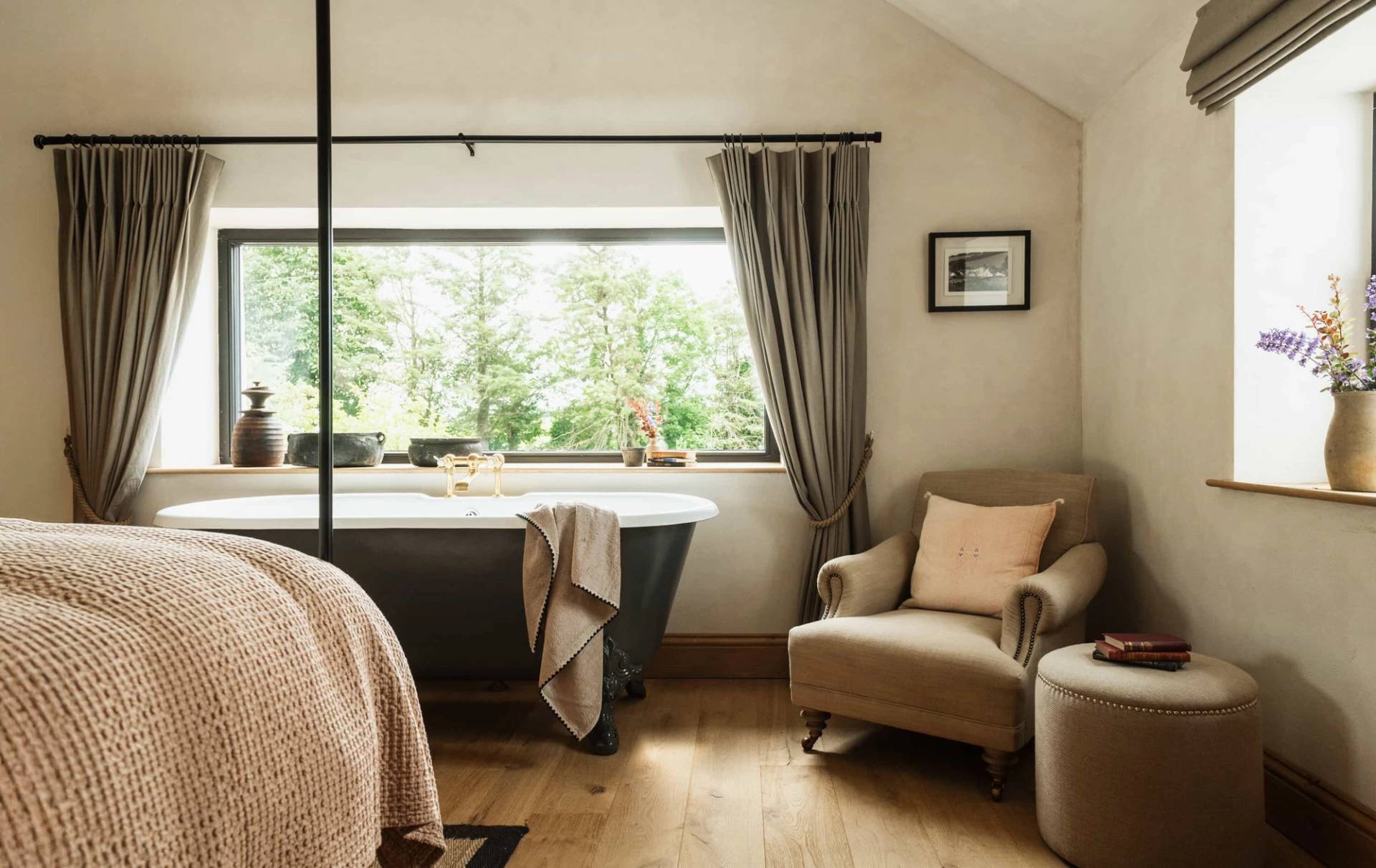 Country bedroom film location in Castleblayney County Monaghan Ireland through Love Locations, featuring a dark freestanding roll-top bath next to a garden view window.