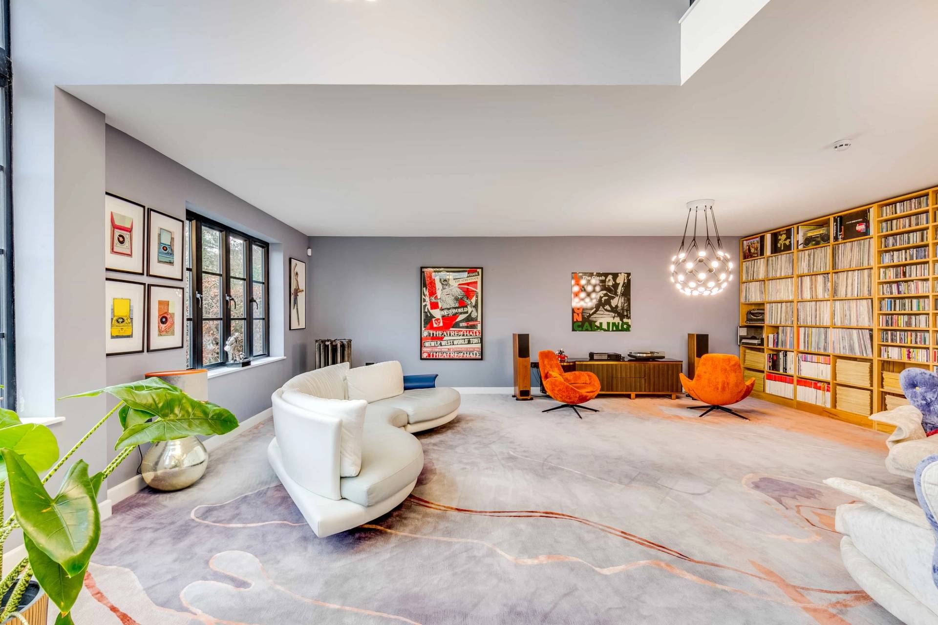 Spacious lounge room with curved white sofa, rainbow accent chairs, and floor-to-ceiling bookshelf wall, Love Locations CB2.