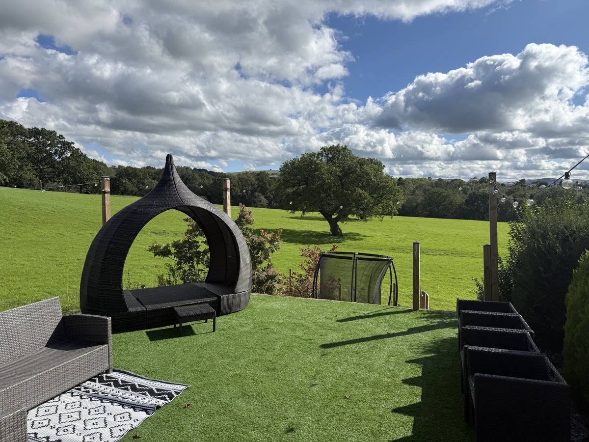 Private garden terrace with artificial lawn, outdoor pod seating, and countryside views in Stockport SK6 by Love Locations.