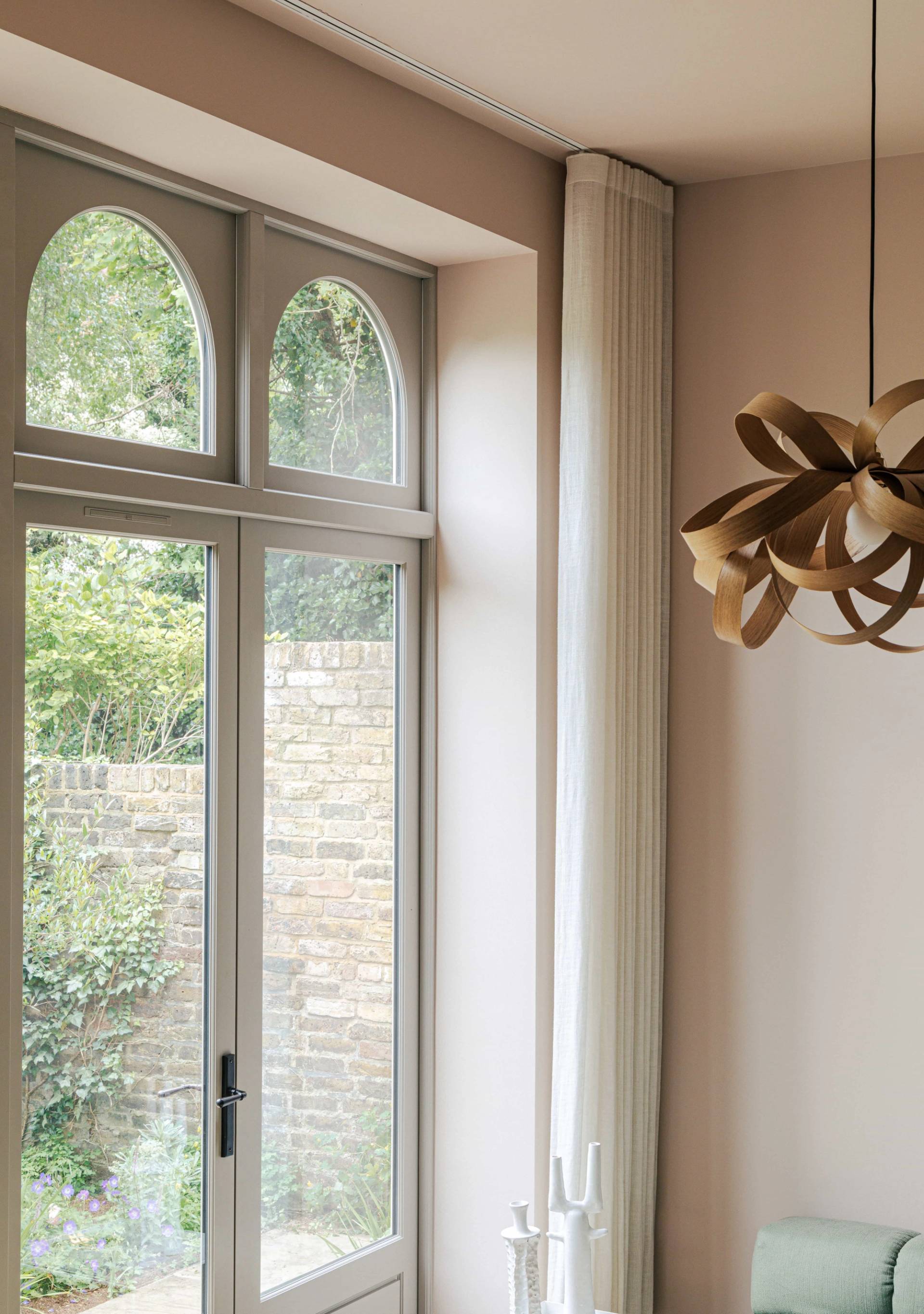 Architectural view of tall arched window frames overlooking brick garden walls in a Barnes location home, Love Locations.
