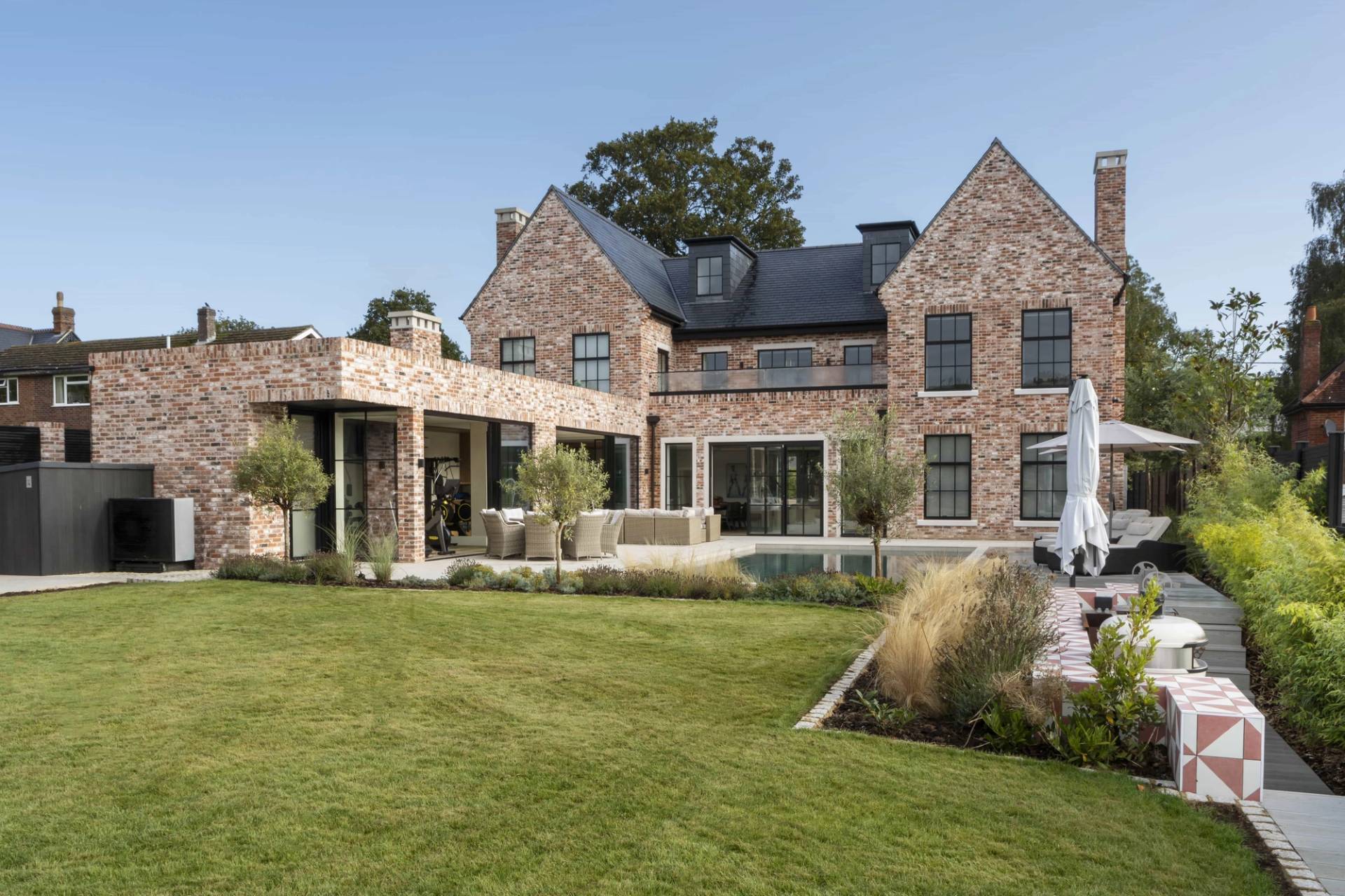 Landscaped lawn garden view looking towards a luxury red brick country home with outdoor pool, Love Locations HP18.
