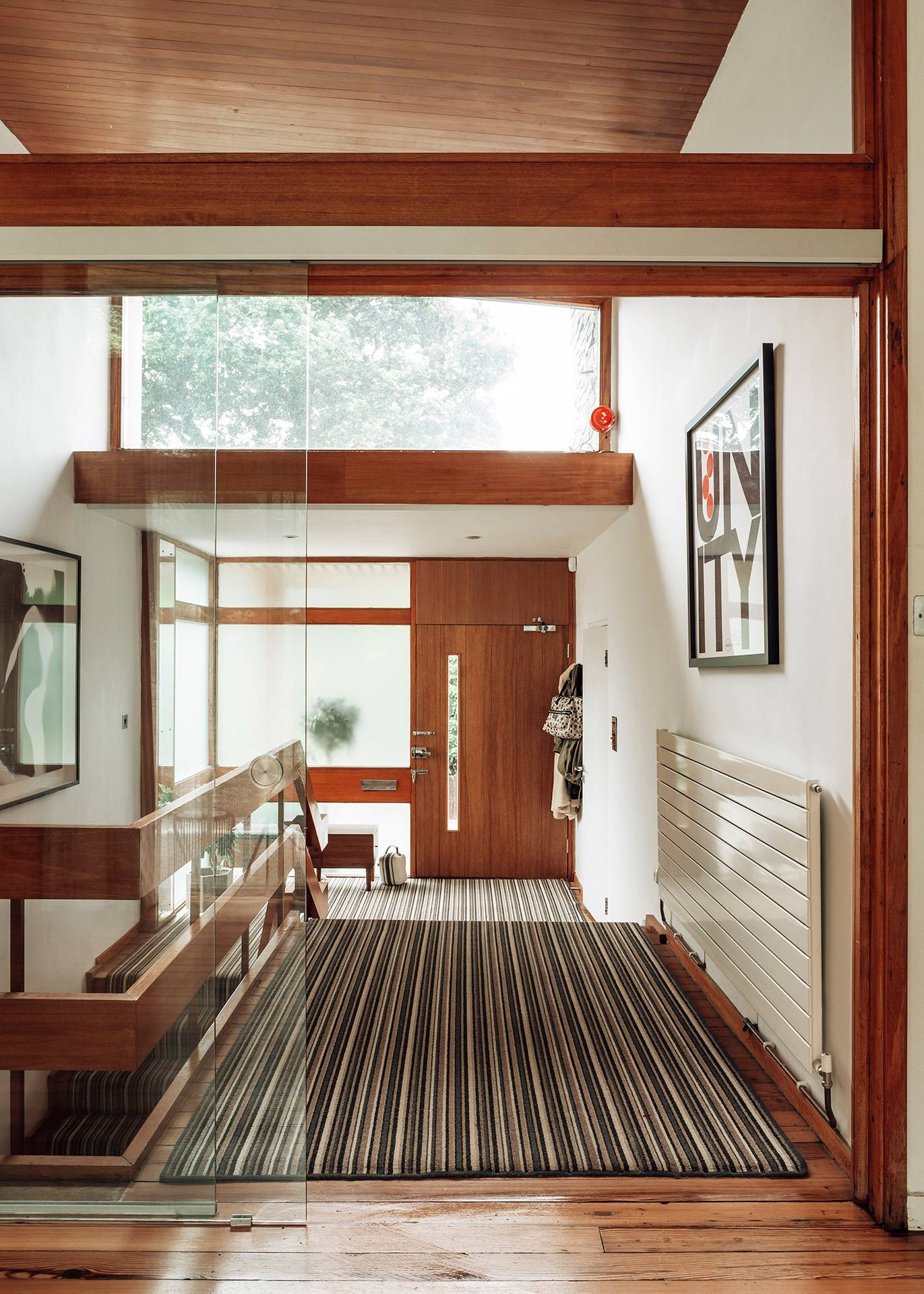 Mid-century modern front entryway featuring a timber-panelled front door, white radiators, and striped hallway runner, Love Locations.