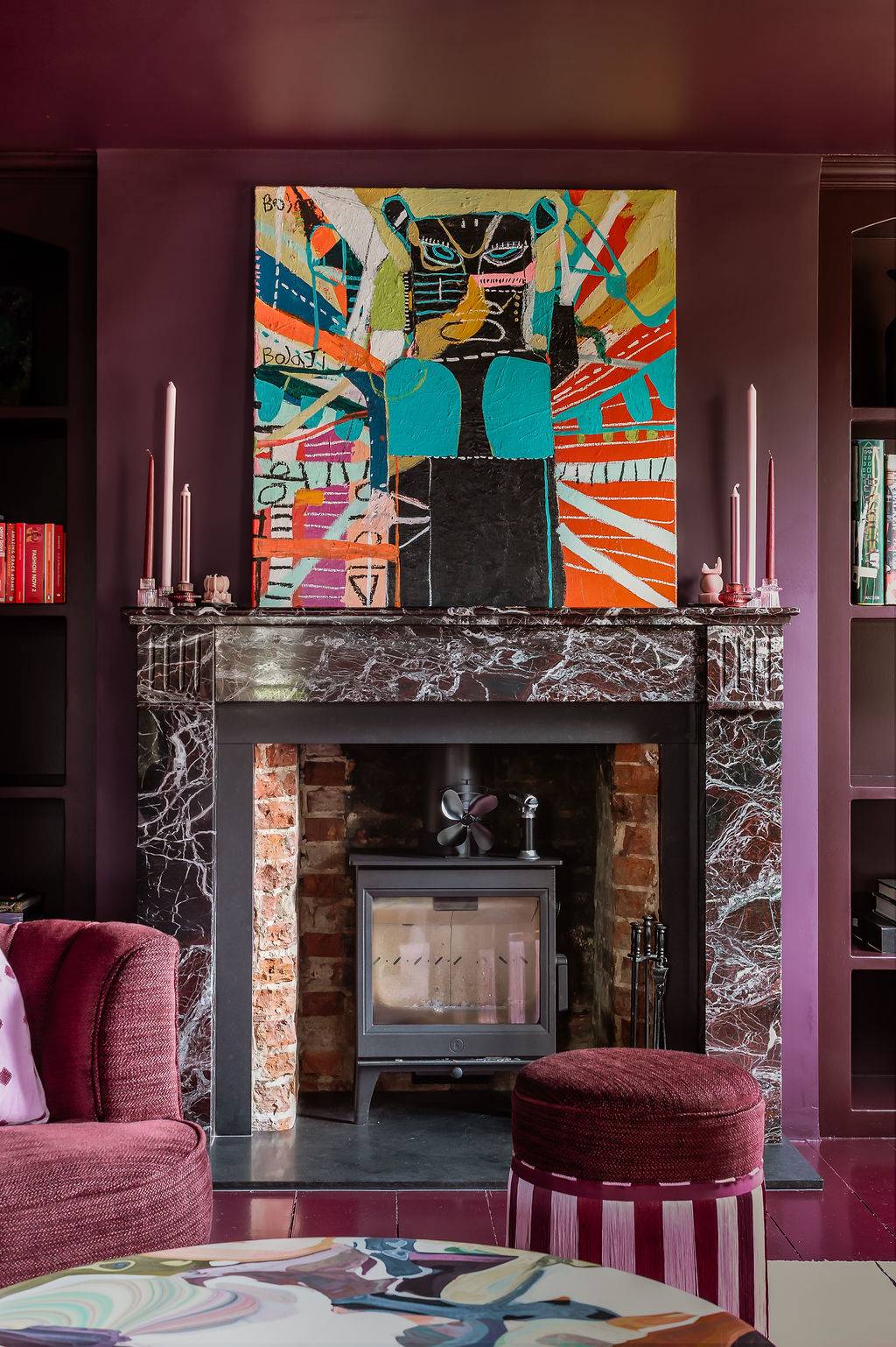 Ornate dark marble fireplace mantle underneath an abstract colorful canvas painting in a moody library layout by Love Locations.