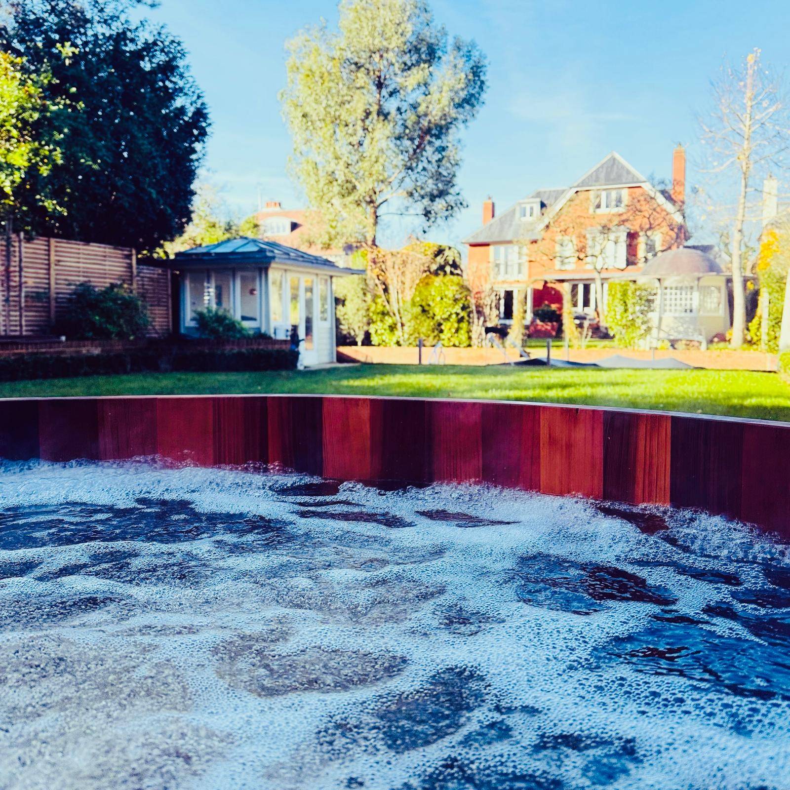 View across a sunken terrace and swimming pool looking towards a red-brick Victorian house facade, Love Locations TW11.