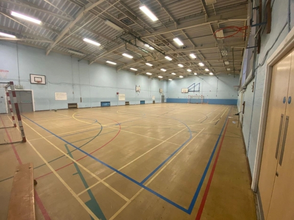 Love Locations commercial sports hall backdrop CM1: Multi-use indoor court mapping out basketball and football lines under an industrial ceiling, excellent for sports apparel branding and music videos.