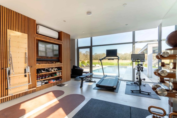 Love Locations professional home gym shoot space Godalming Surrey: High-tech fitness suite showing a treadmill and workout benches facing clear pool courtyard views, ideal for sports brand ads.