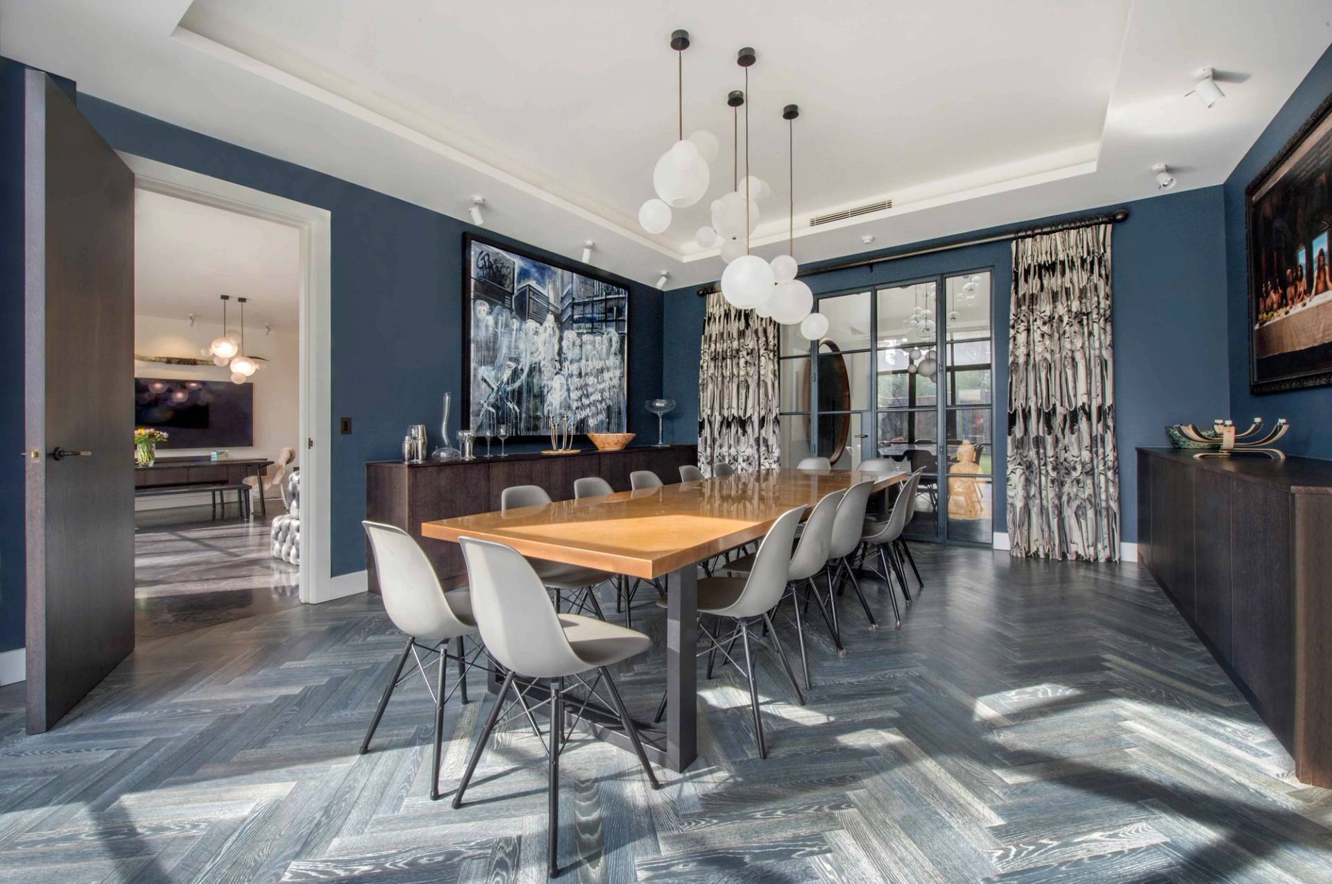 Formal dining room setup featuring a large wooden table, modern grey chairs, patterned curtains, and rich blue accent walls, Love Locations NW3.
