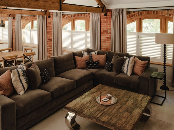 Cozy corner sofa layout with a rustic wooden coffee table and brick feature wall inside a Nuffield barn location, ideal for casual apparel campaigns, Love Locations RG9.