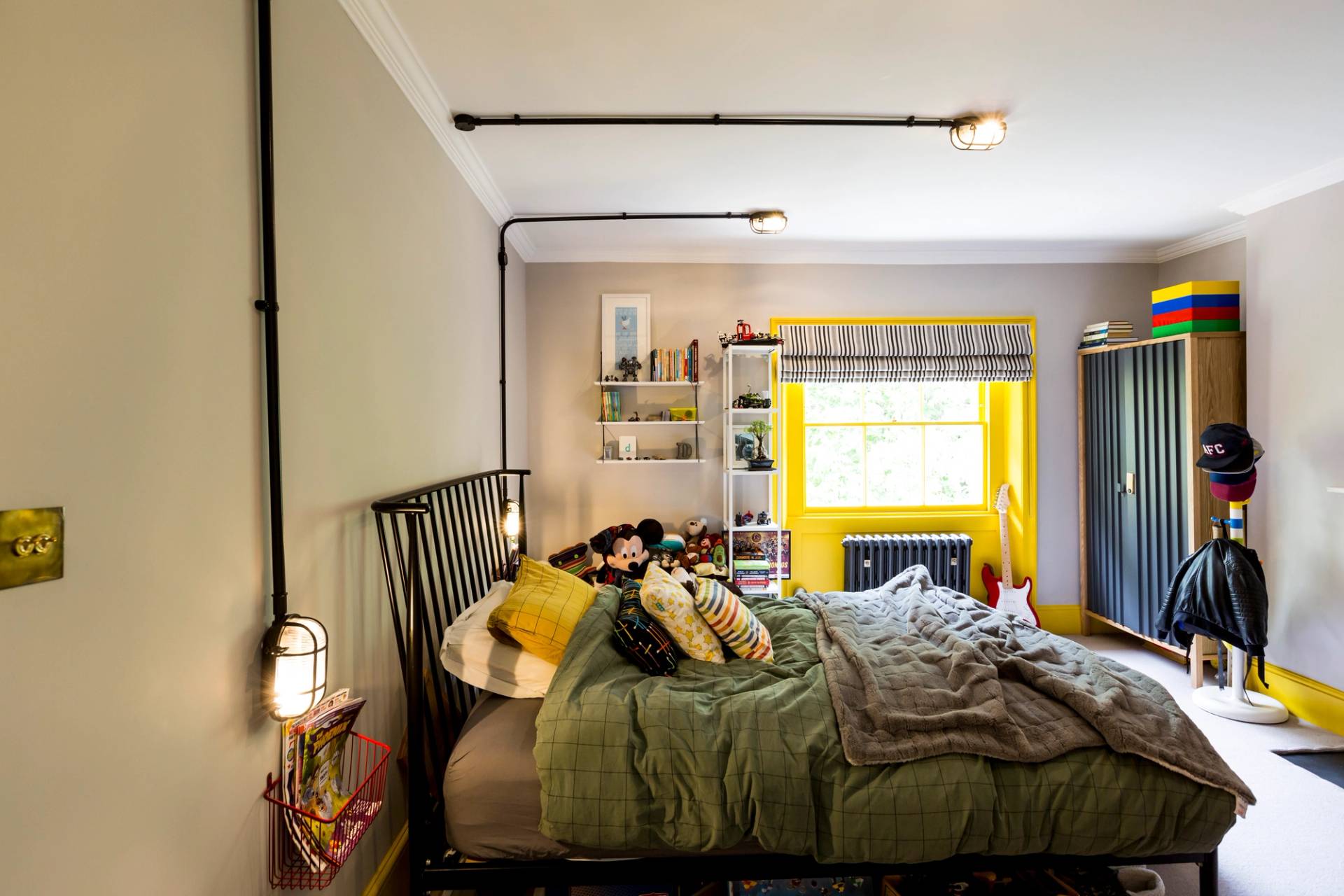 Eclectic bedroom with industrial exposed conduit lighting, yellow window frame, and olive walls in SE5 via Love Locations.