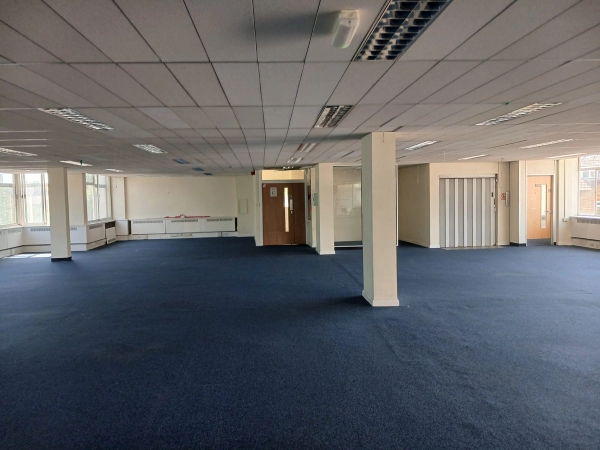 Deserted commercial building location for photoshoot hire in Watford WD18 by Love Locations, displaying a wide corporate room with blue carpet and structural concrete pillars.