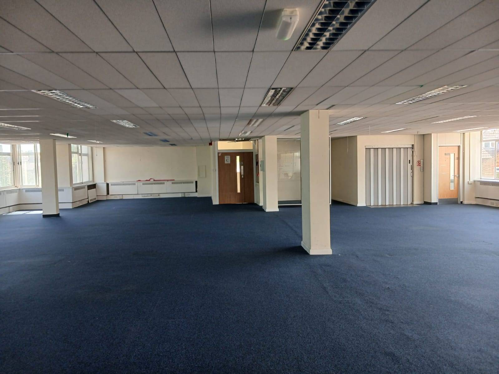 Deserted commercial building location for photoshoot hire in Watford WD18 by Love Locations, displaying a wide corporate room with blue carpet and structural concrete pillars.
