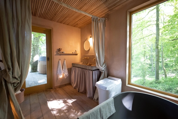 Sunlit rustic bathroom suite showcasing an open glass door leading directly out to a private woodland forest terrace, Love Locations HR4 8ls.