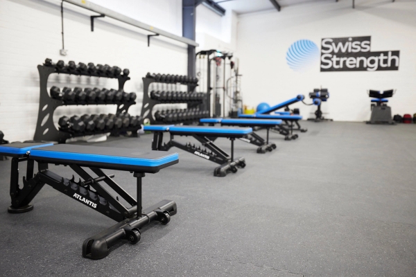 Adjustable workout benches paired with rows of free weight dumbbell racks in a clean, brightly lit fitness facility, Love Locations.