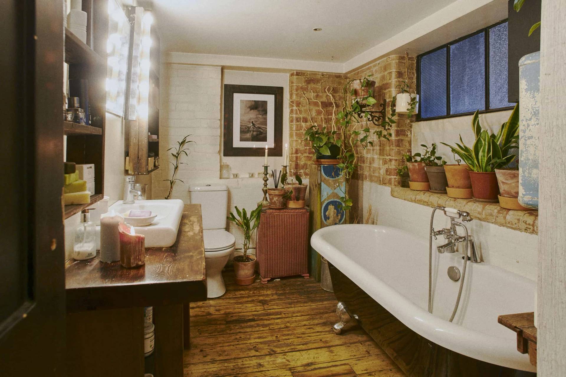 Industrial warehouse bathroom location featuring a classic white clawfoot tub, wooden floorboards, and exposed brick walls, Love Locations.