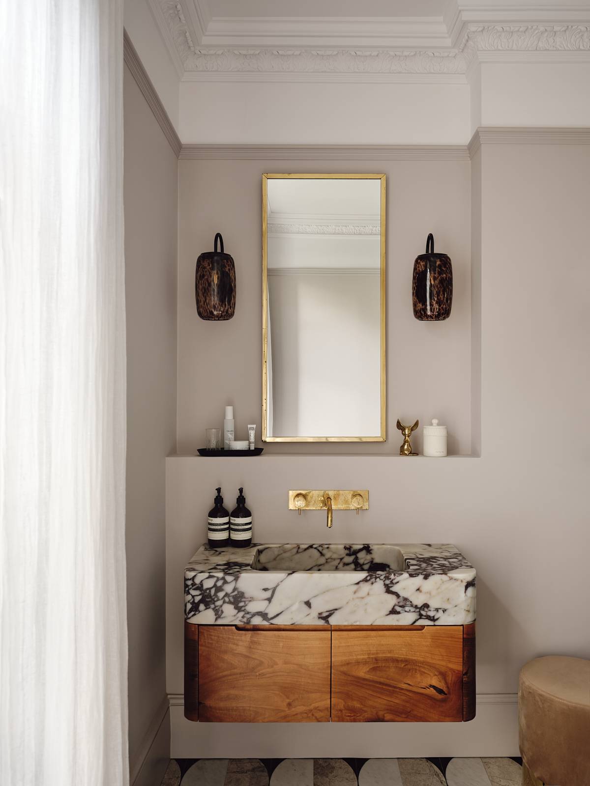 Marble-topped wooden bathroom vanity unit featuring a gold wall tap and brass wall sconces, Love Locations CR0.