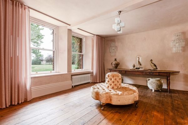 Spacious neutral plaster gallery room featuring a central round yellow tufted ottoman stool, a premium fashion shoot location by Love Locations.