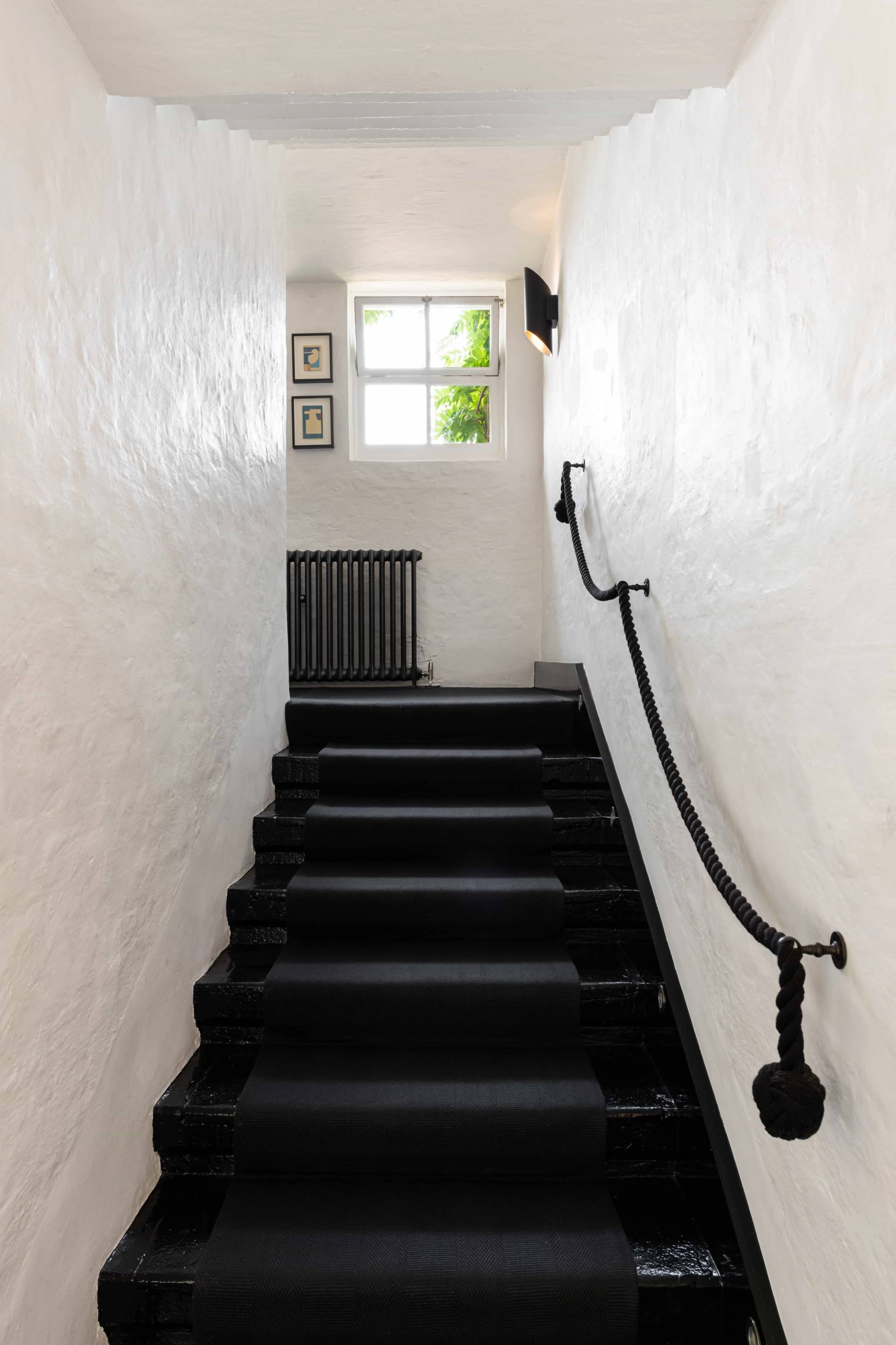 Stark black painted staircase set against rustic white plaster walls with a black metal handrail, ideal for fashion editorial photography, Love Locations.