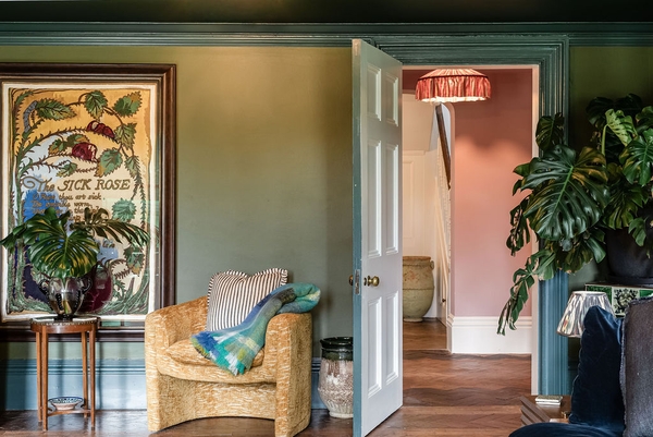 Multi-room perspective view from a green country house salon leading through an open white door into a soft pink hallway via Love Locations.