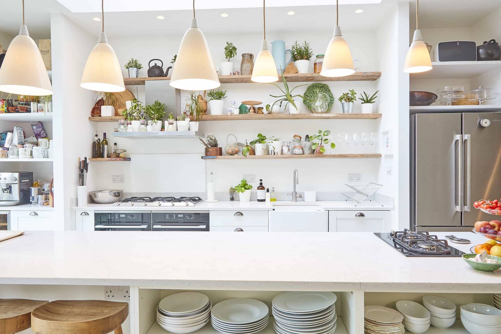 Symmetrical shot of open wooden kitchen shelving styled with ceramics, set above a stainless steel cooker and white island, Love Locations.