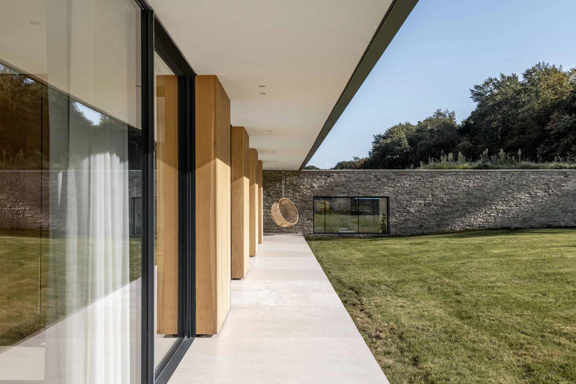 Covered concrete colonnade walkway with timber support pillars framing views of a stone wall boundary and green lawn in Essex, Love Locations CM4.