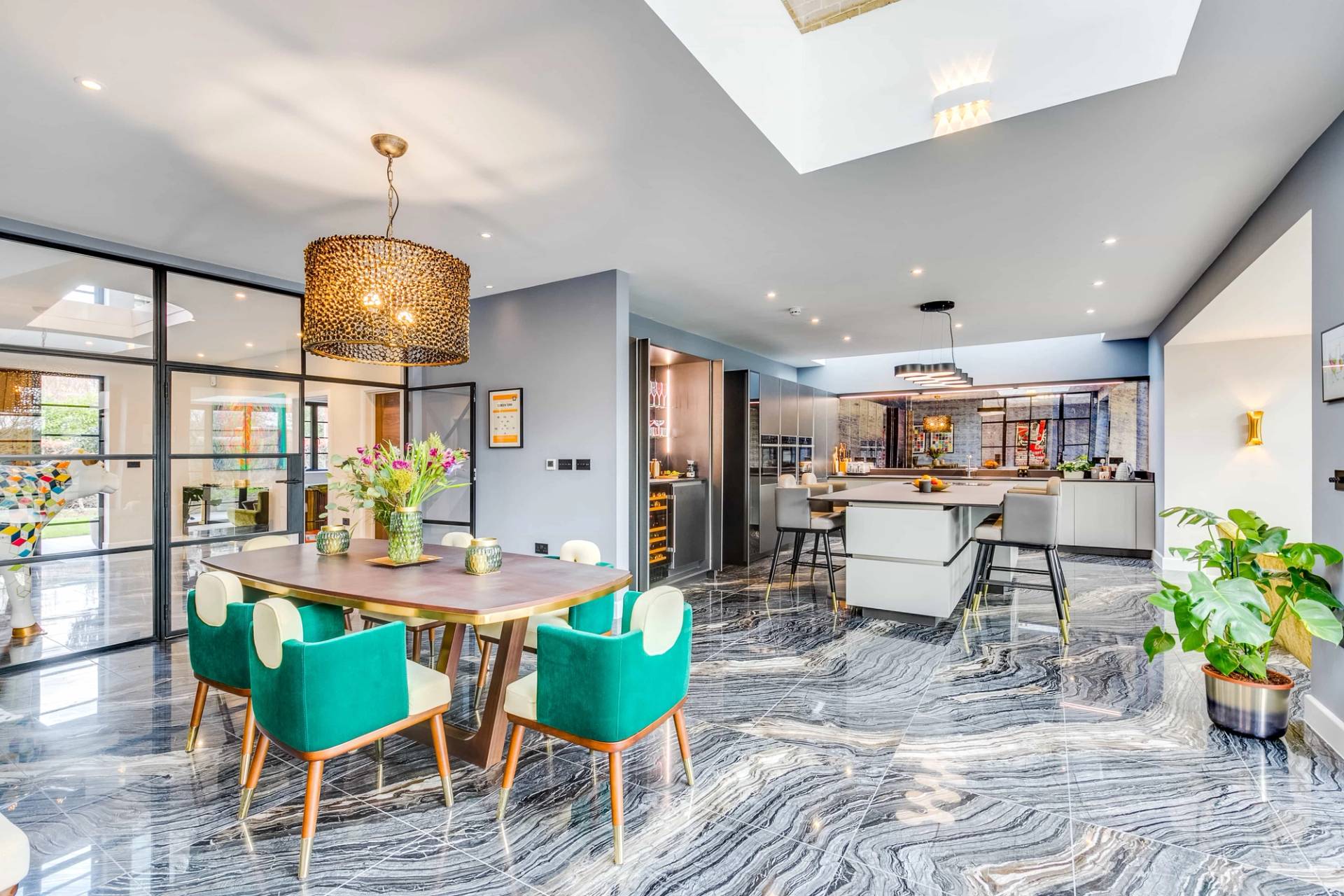 Open-plan reception room view looking from a green velvet dining suite toward a modern kitchen island, Love Locations CB2.