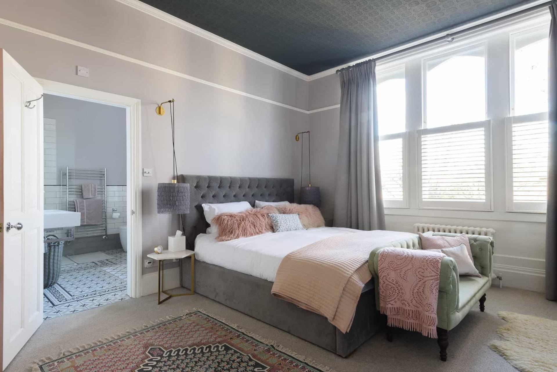 Spacious bedroom suite featuring grey panelled walls, tufted upholstered bed, and sheer window drapes, Love Locations TW11.
