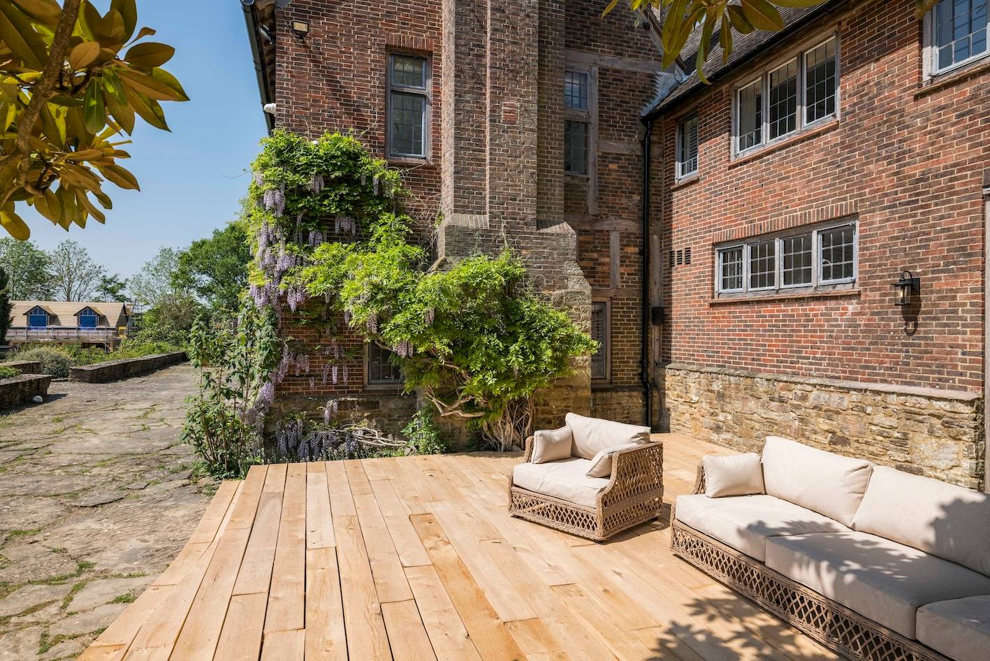 Elevated wooden deck patio with outdoor lounge chairs set beside climbing vines and brick mansion walls, Love Locations RH13.