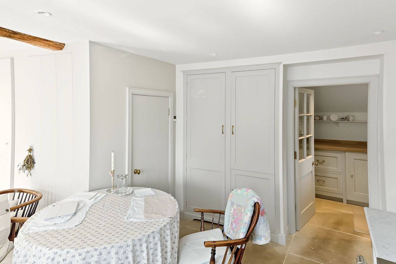 Bright white cottage dining nook shoot location in Gloucestershire GL7 by Love Locations, displaying fitted linen cupboards and a traditional round table setup.