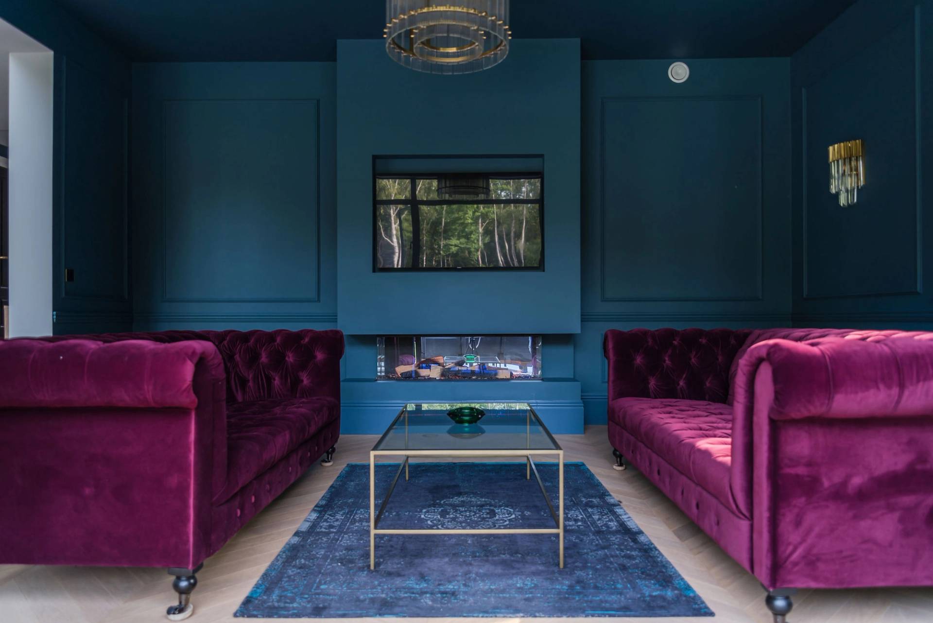 Moody dark teal reception room featuring twin deep purple velvet chesterfield sofas, blue rug, and modern inset fireplace, Love Locations GU3.