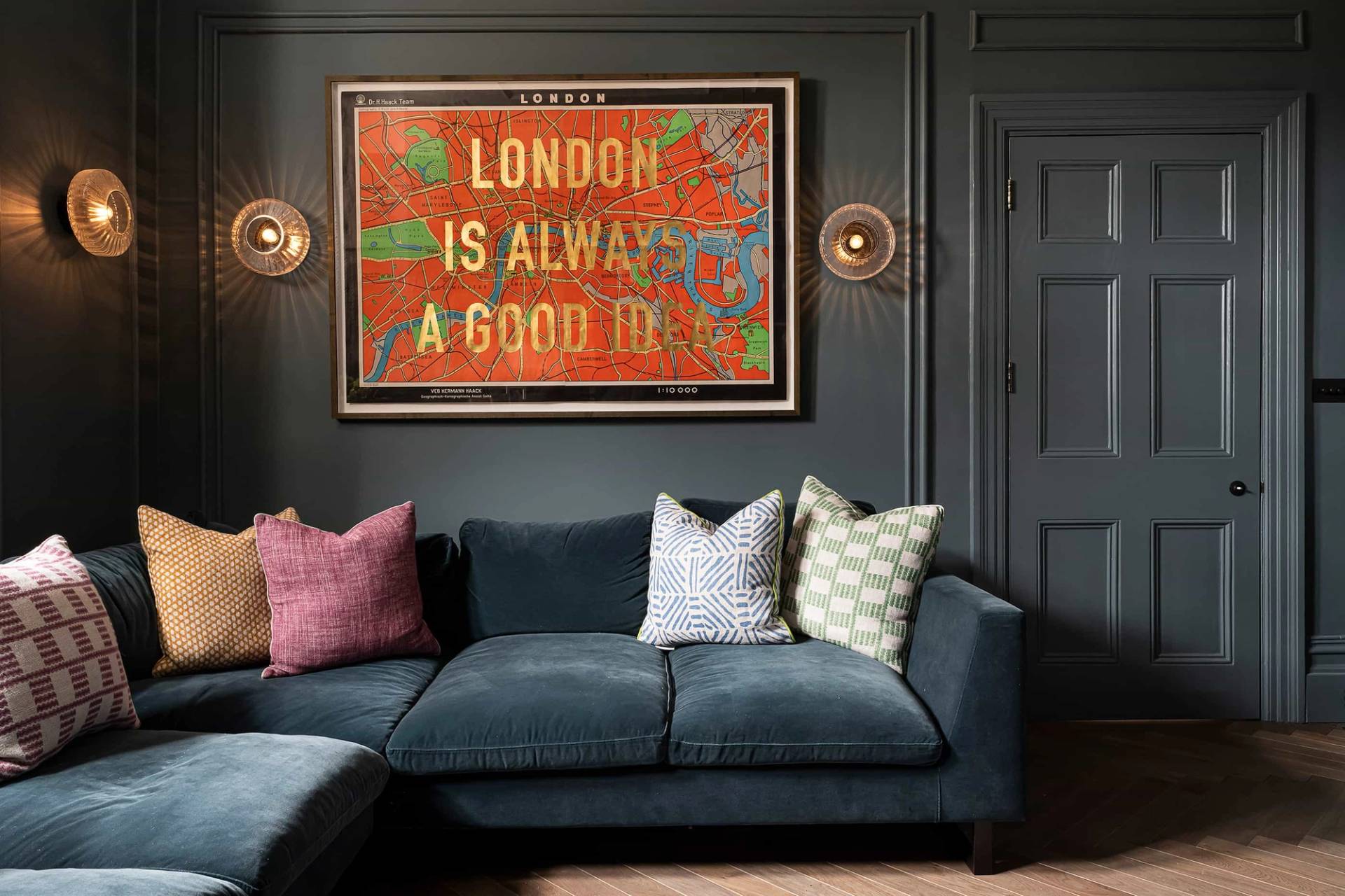 Dark teal TV room featuring a London statement art print, velvet corner sofa, and brass sconces, Love Locations NW6.