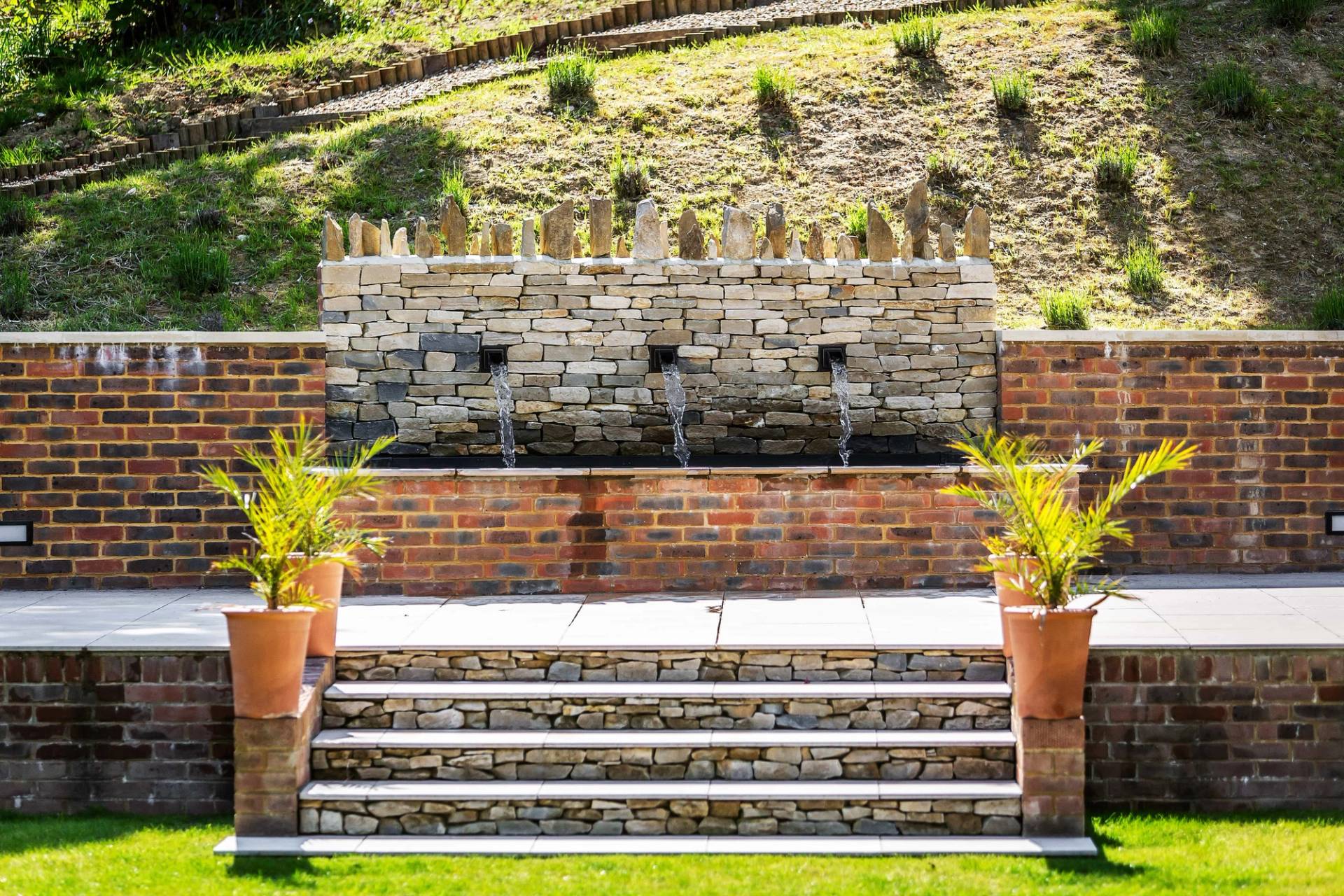Bespoke stone wall water feature cascading into a garden pond in a private Surrey estate, Love Locations.