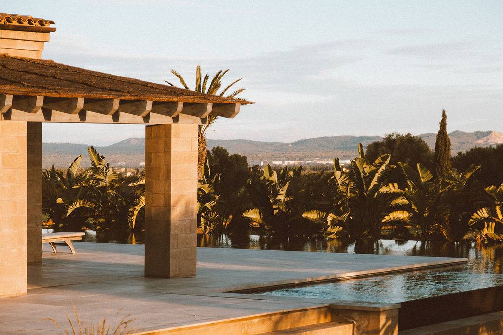 Sunlit infinity pool terrace with stone pillars looking out across Mallorcan mountain horizons, Love Locations 07630.