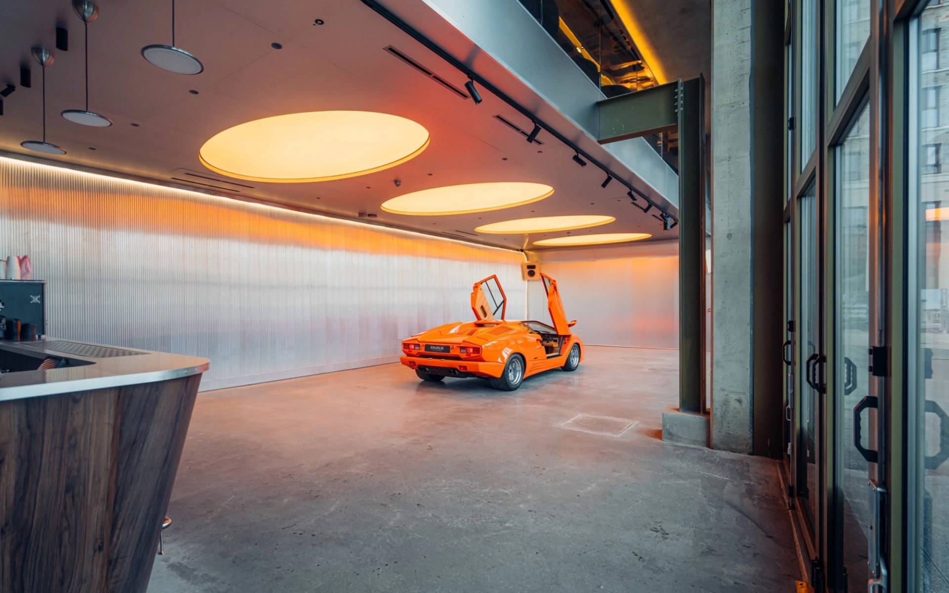Bright orange Lambo parked on polished concrete under circular ceiling lighting inside Plonkers Listening Bar in Brentford TW8 by Love Locations.