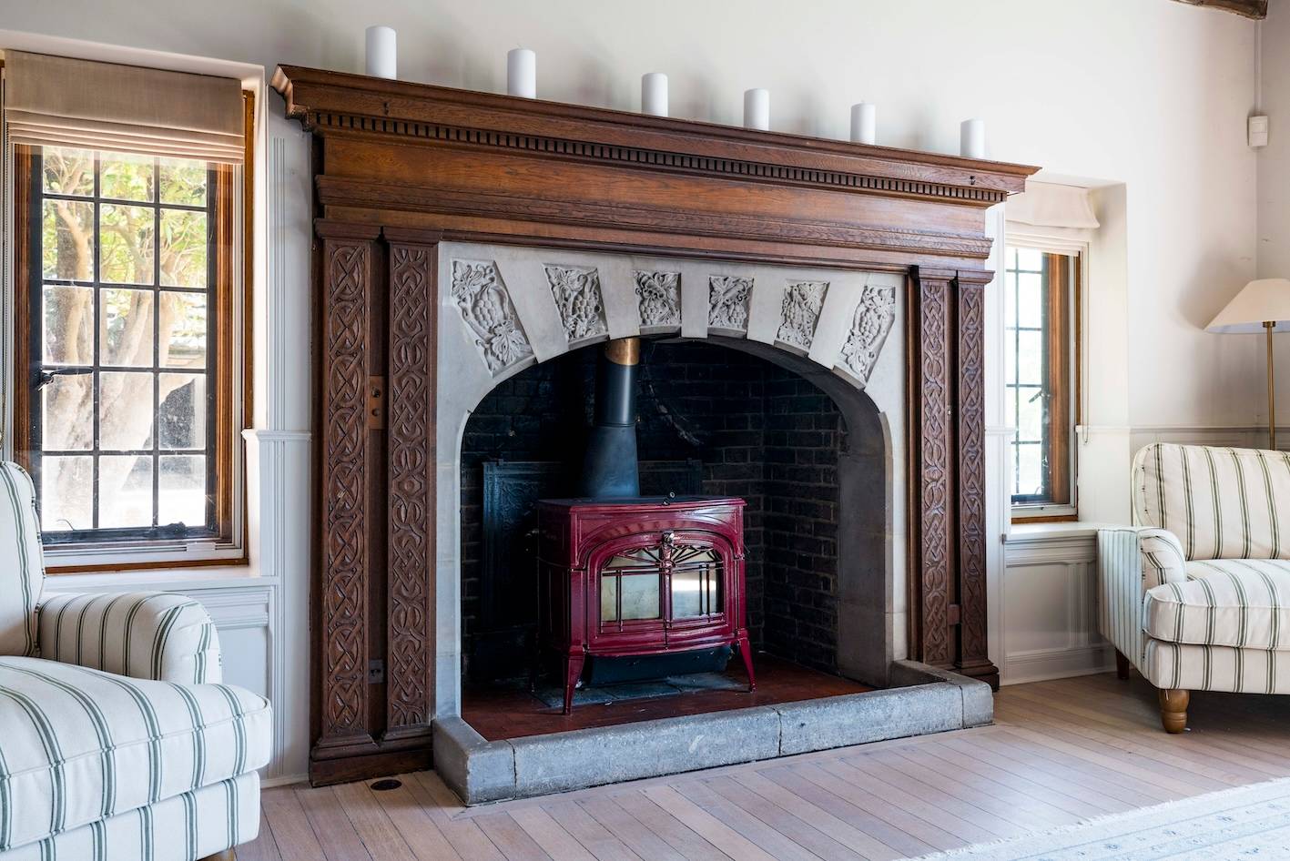 Carved oak fireplace surround with dark brick alcove and red wood-burning stove, Love Locations RH13.