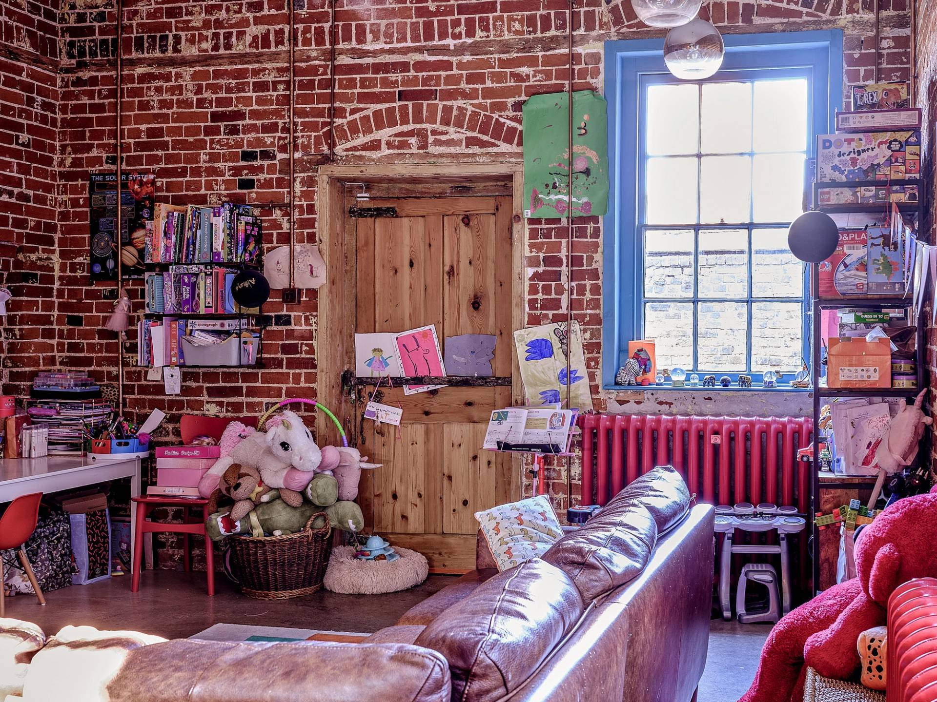 Cozy brick-walled snug room featuring a brown leather sofa, blue sash window frames, and rustic timber doors, Love Locations.
