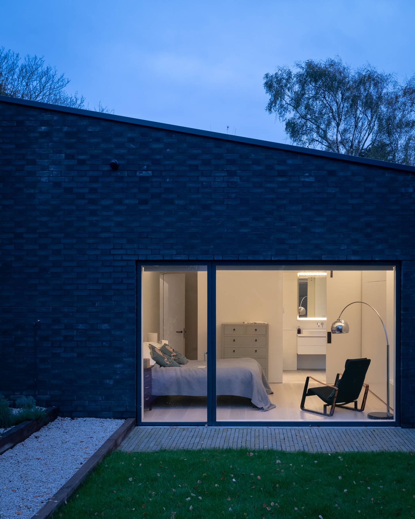 Illuminated bedroom window view glowing against a dark grey brick house facade at twilight, Love Locations BN3.