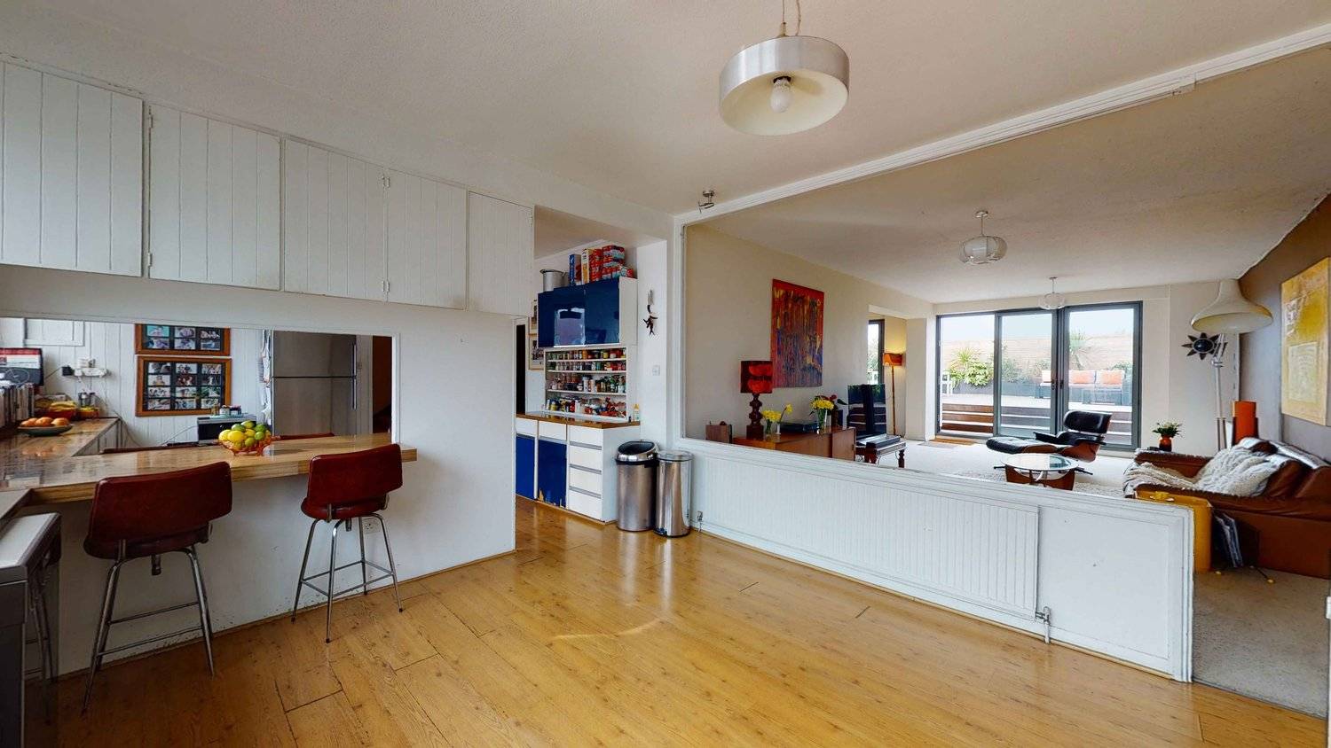 Open-plan kitchen view looking across a wooden breakfast bar into a bright 1970s reception room, Love Locations SW16.