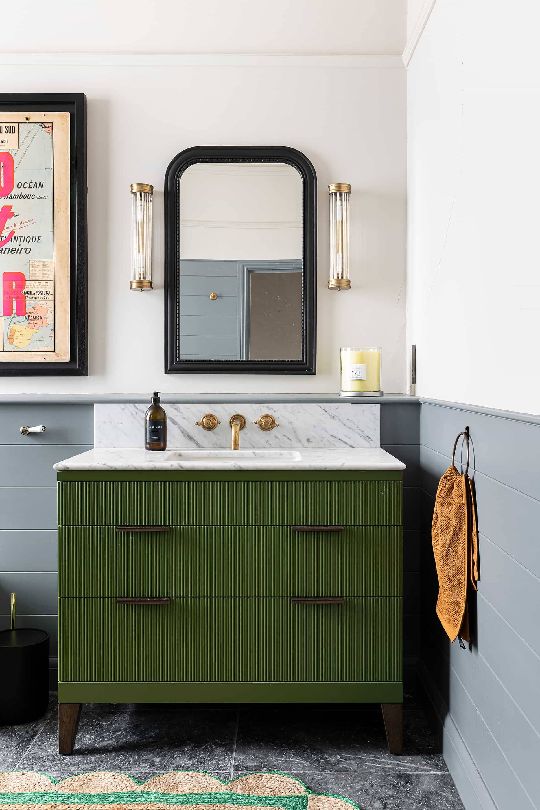Dark green ribbed bathroom vanity cabinet set against grey panelled wainscoting and a rounded black mirror, Love Locations NW6.