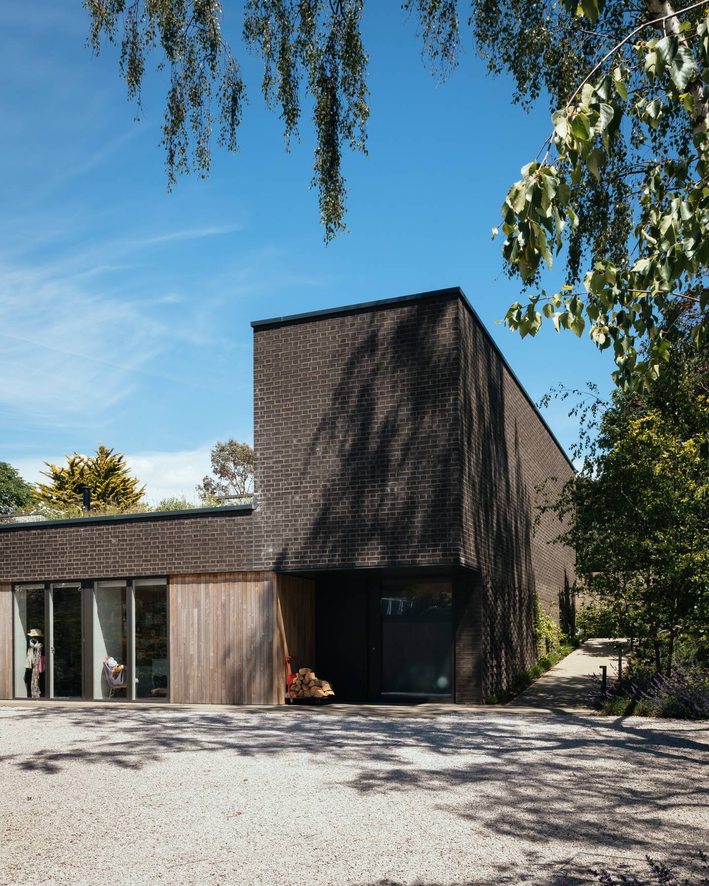 Architectural front elevation showing dark brick cladding, timber accents, and gravel driveway, Love Locations BN3.