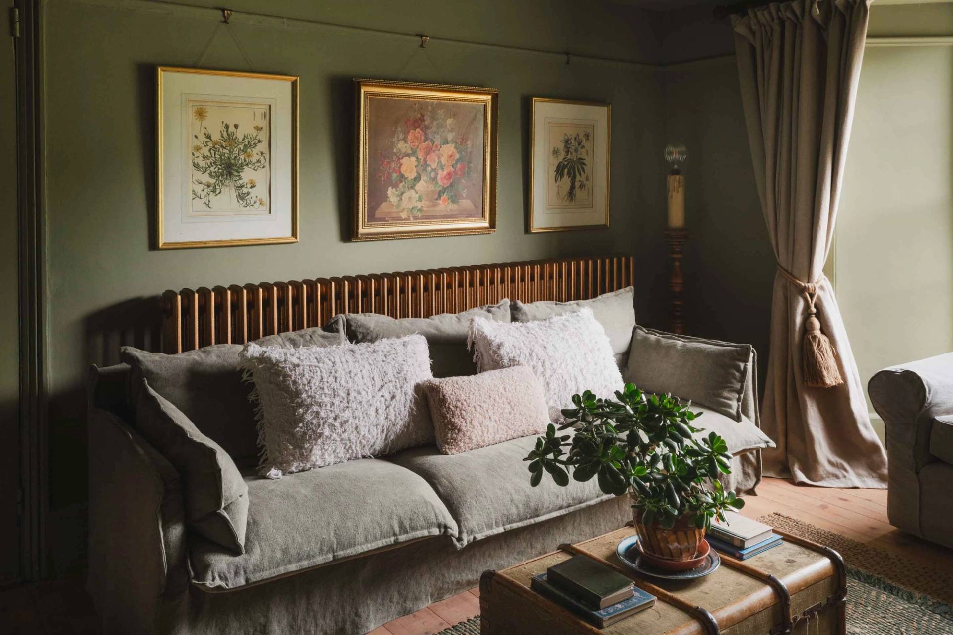 Olive green sitting room location house in Newquay Cornwall from Love Locations, featuring a plush grey sofa, framed botanical art, and timber wall detailing.
