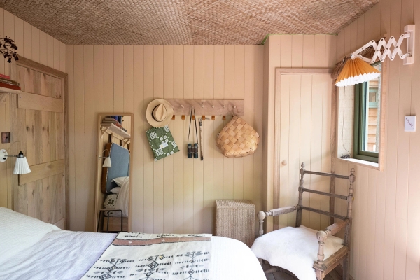 Minimalist bedroom dressing area backdrop with a simple wooden chair, wall pegs, and hanging woven straw bags, curated by Love Locations.
