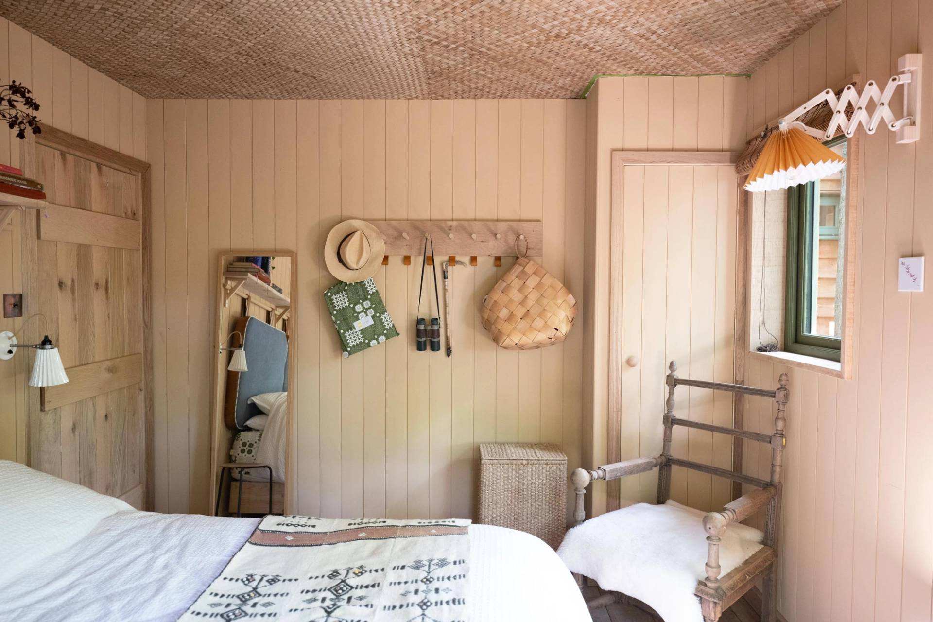 Minimalist bedroom dressing area backdrop with a simple wooden chair, wall pegs, and hanging woven straw bags, curated by Love Locations.