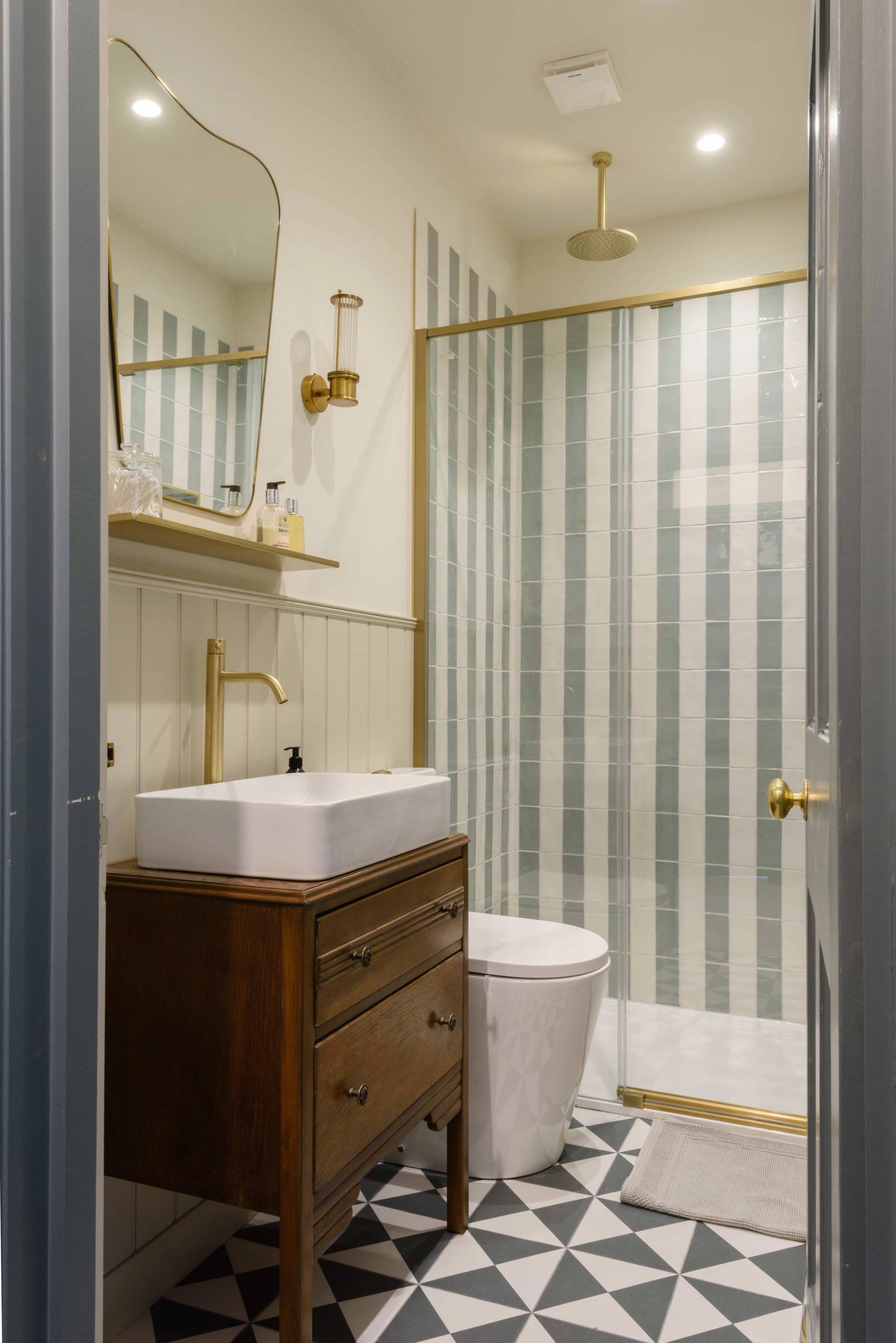 Shower room vanity unit featuring a rectangular vessel sink, wooden cabinet, and striped shower curtain, Love Locations TW11.