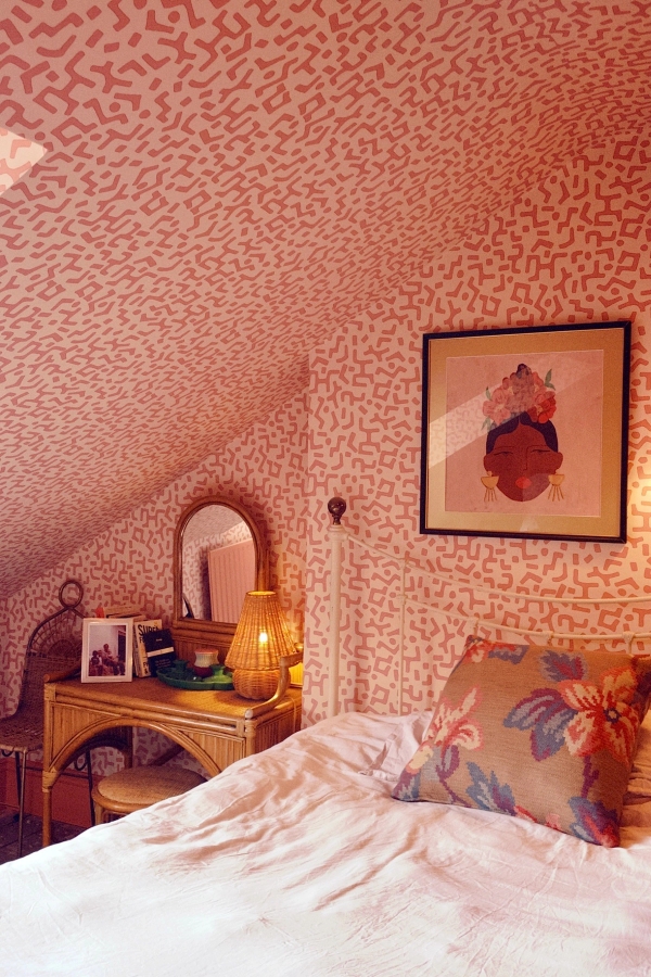 Cozy attic bedroom with pink patterned wallpaper, a rustic wooden vanity, and framed wall art, ideal for youth lifestyle brand shoots, Love Locations.