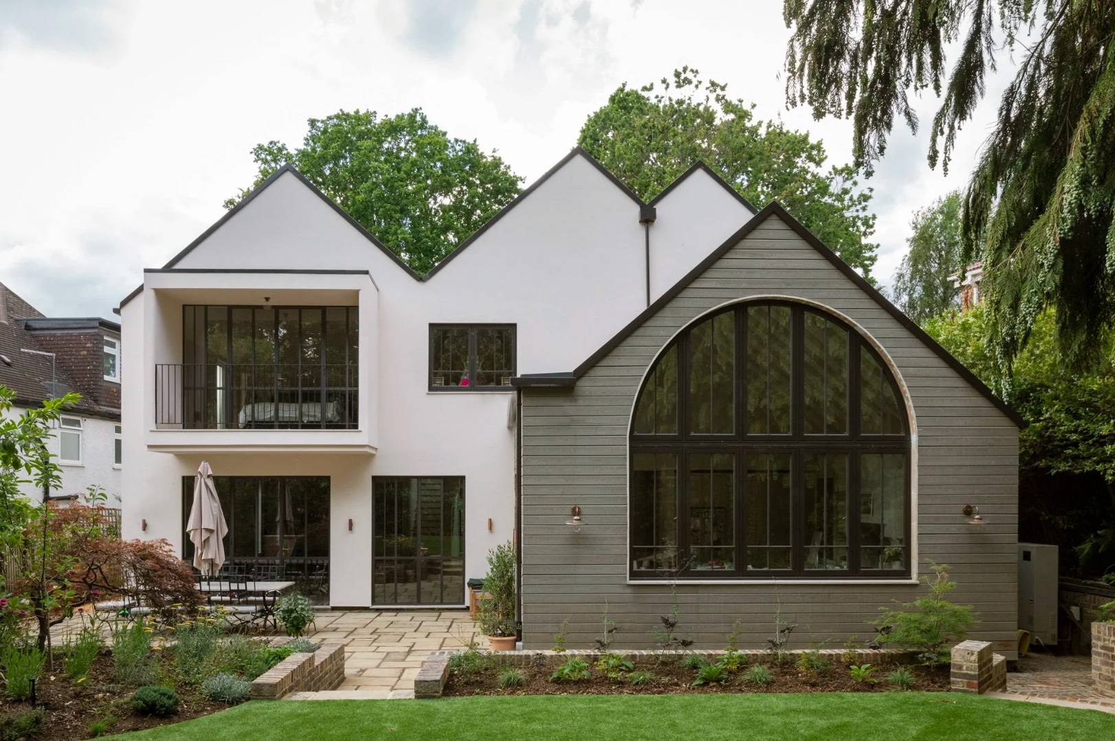Rear exterior facade establishing shot of a white and grey gabled house in Fortis Green, N6 featuring a grand arched window and landscaped patio garden, the ultimate hero backdrop for TV drama filming, luxury car ads, and commercial productions via Love Locations.
