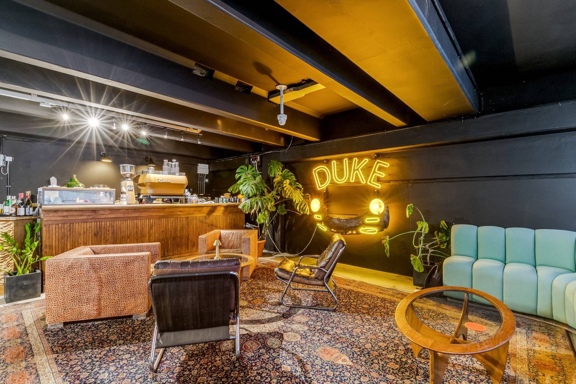 Mid-century style lounge and coffee bar filming space in a Brentford car showroom through Love Locations, with yellow neon signage and potted tropical plants.