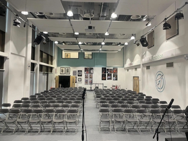 Love Locations school assembly hall Reading RG30: Deep presentation space filled with organized seating under industrial studio lighting, perfect for institutional events and theatre scenes.