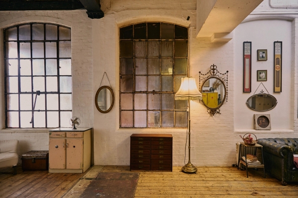 Industrial warehouse corner featuring a large multi-pane factory window, a floor lamp, and a vintage chest of drawers for lifestyle filming, Love Locations EN5.